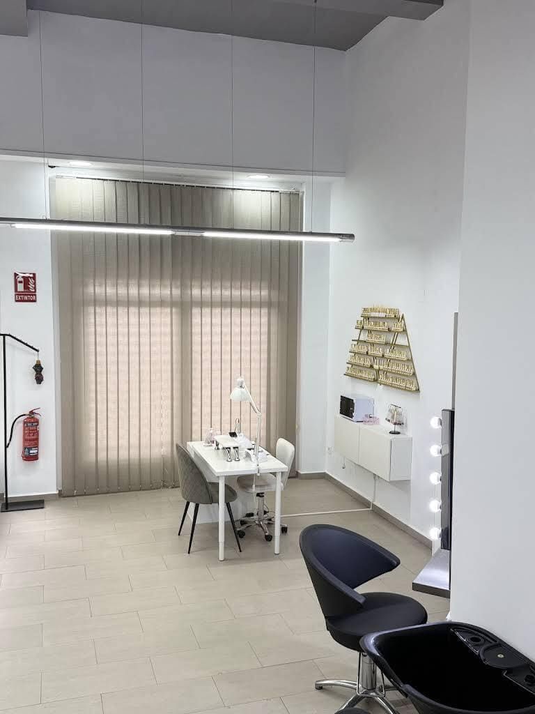 Pequeña oficina blanca con mesa, sillas, cortinas transparentes, cuadros en la pared y un extintor.
