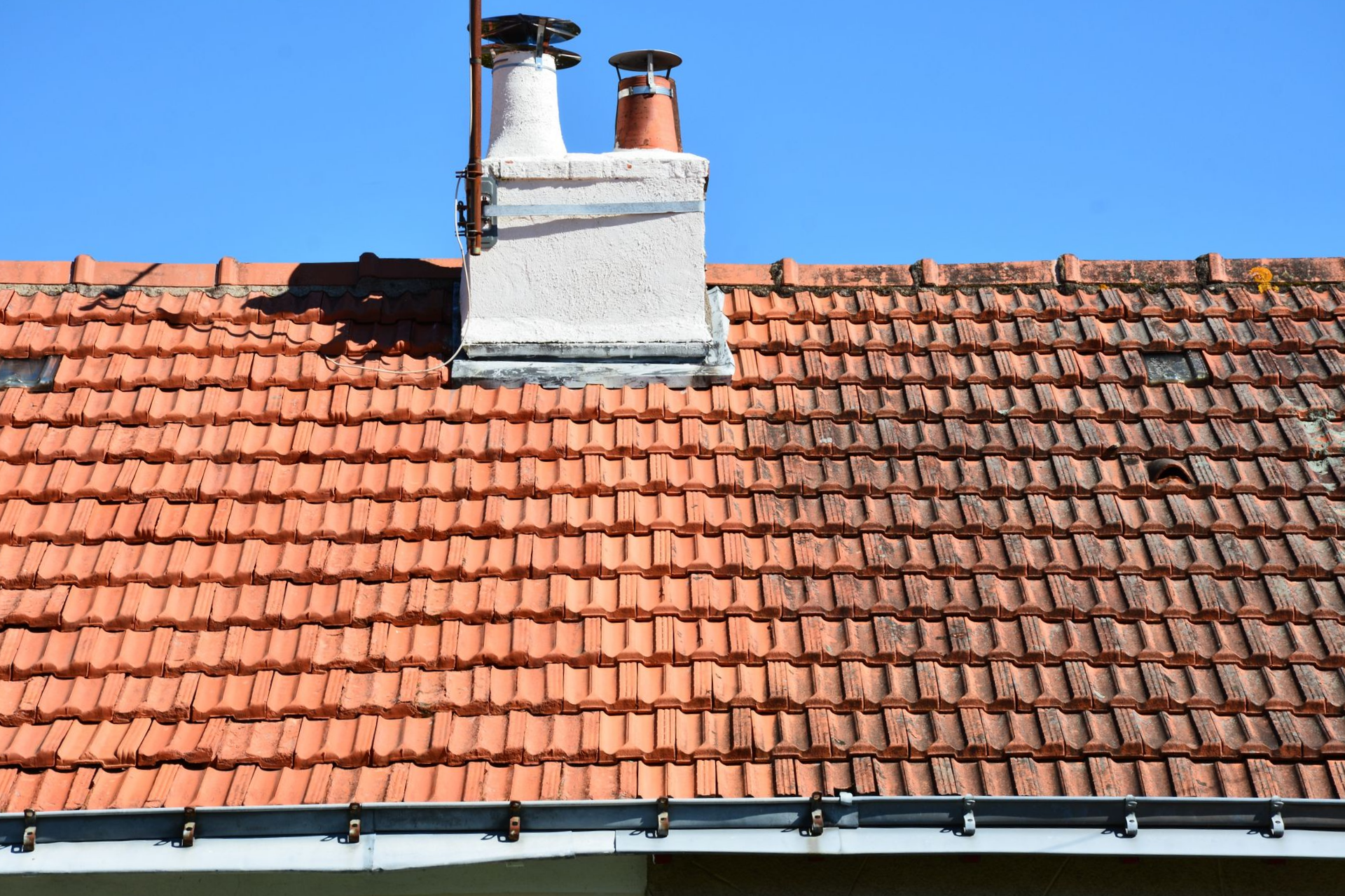 Toit de tuiles rouges avec cheminée et antenne sur un ciel bleu clair.