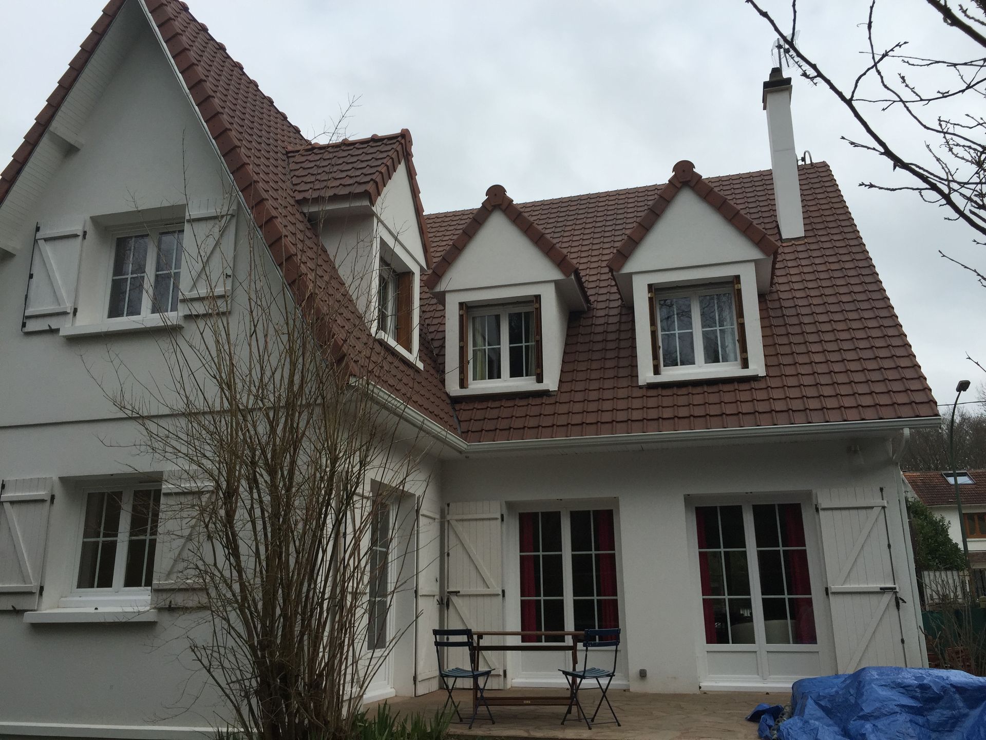 Maison blanche avec toit de tuiles rouges, lucarnes et volets blancs.