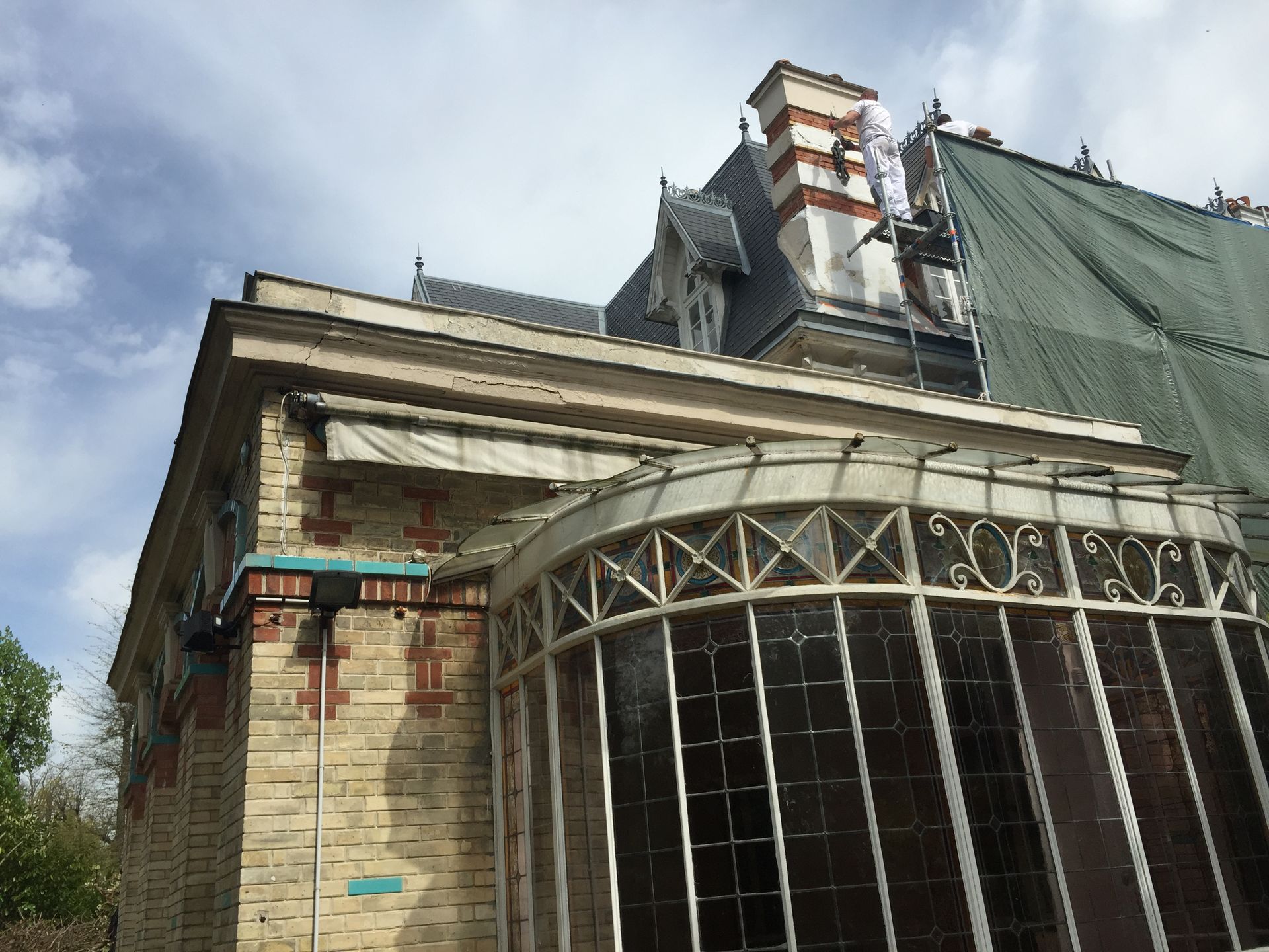 Vue extérieure d'un bâtiment historique en briques, doté d'une enveloppe de verre incurvée et d'une toiture ornée, sous un ciel nuageux.