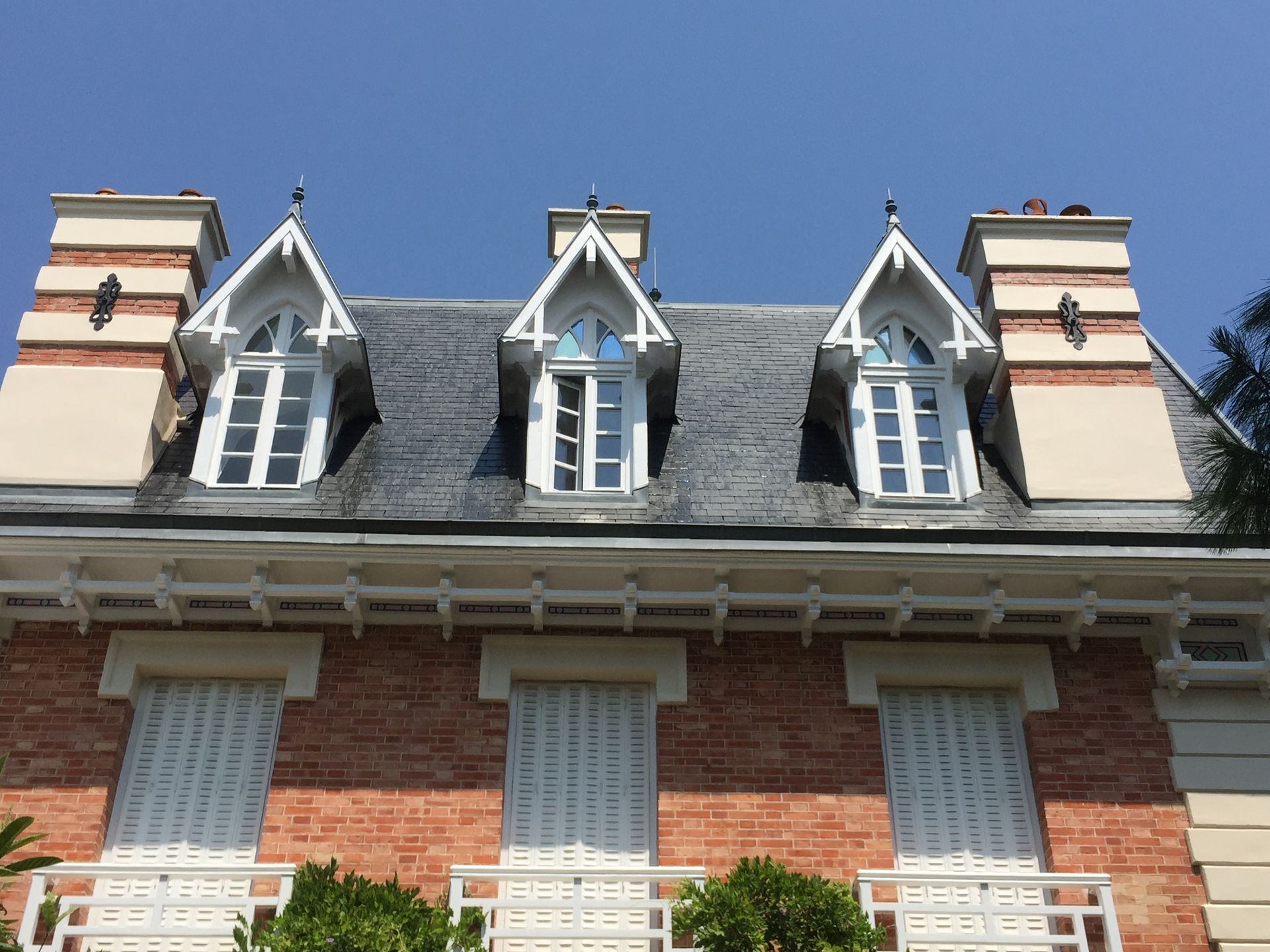 Bâtiment en briques rouges avec des boiseries blanches, des lucarnes et un toit sombre se détachant sur un ciel bleu.
