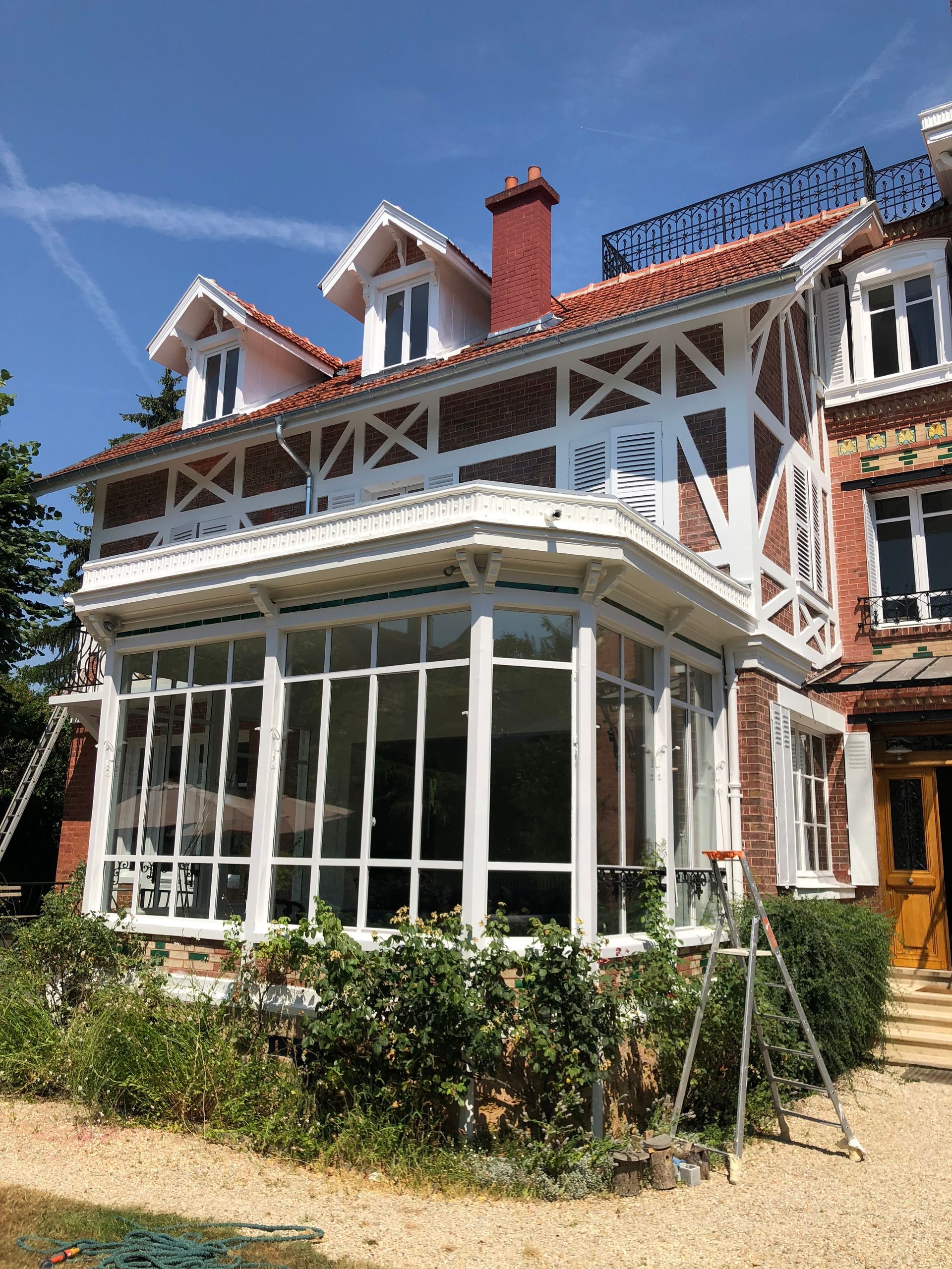 Maison en briques blanches et rouges avec une véranda vitrée sous un ciel d'un bleu éclatant.