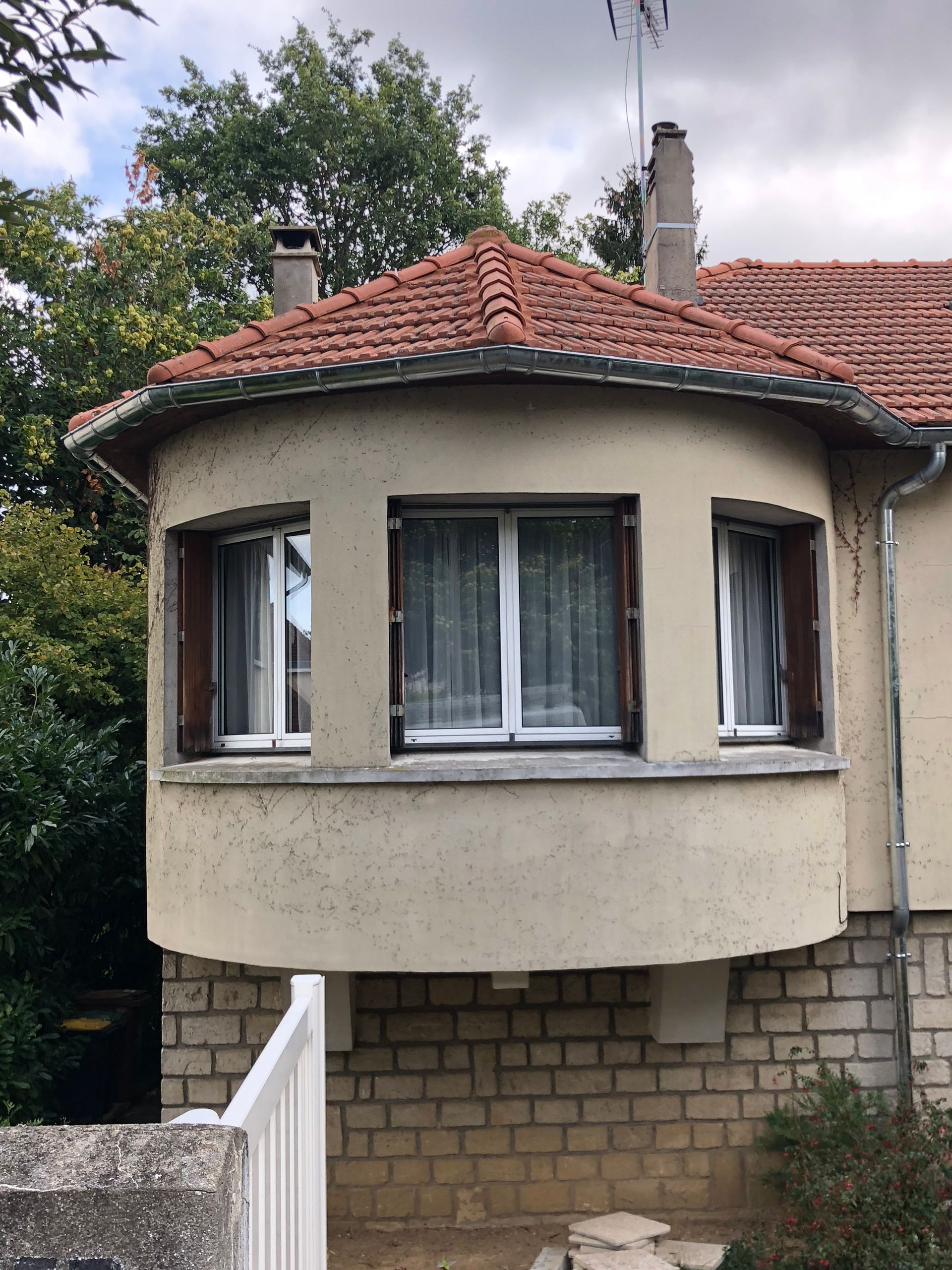 Extension arrondie du bâtiment avec trois fenêtres, toit de tuiles rouges et soubassement en briques.