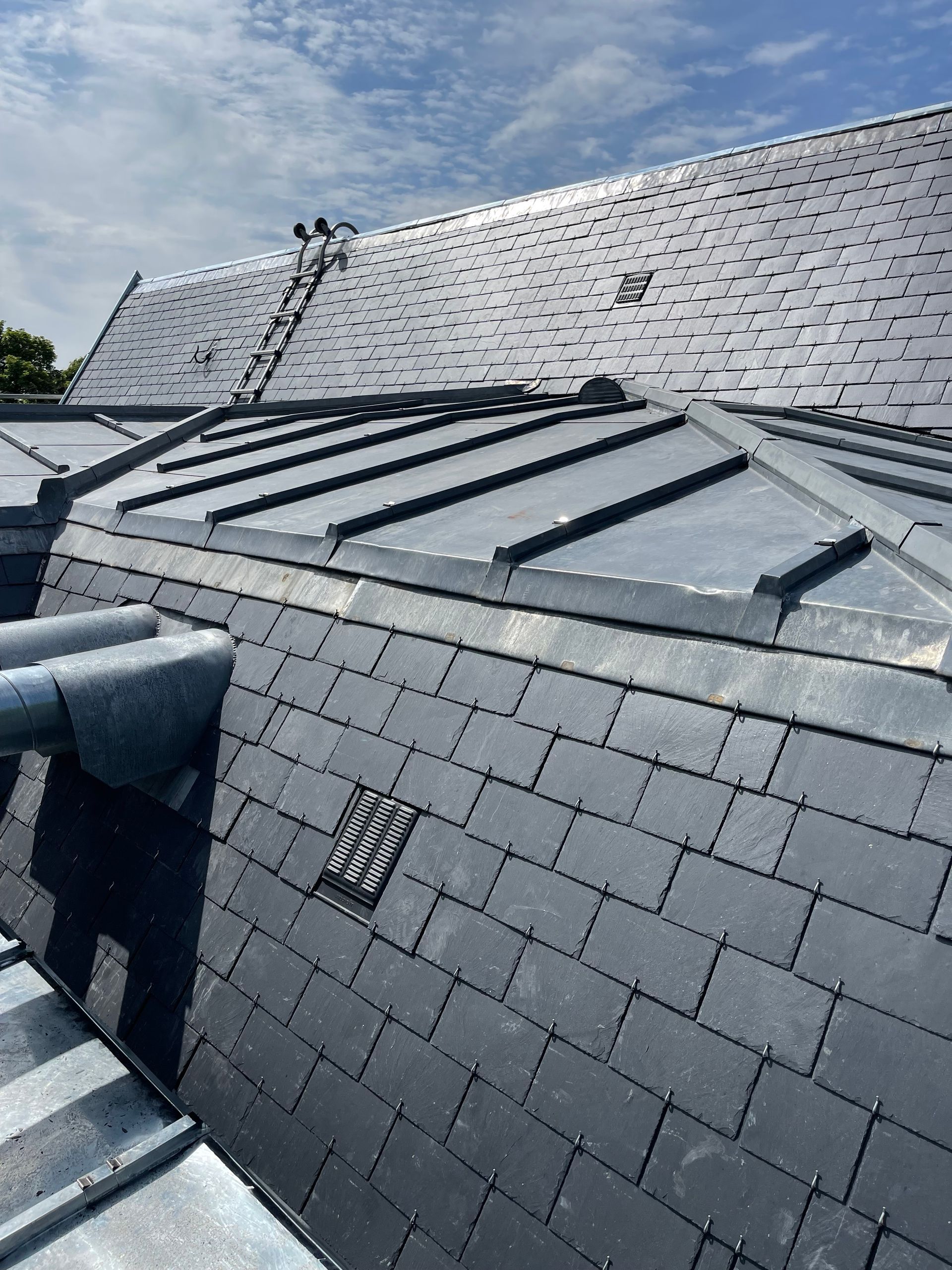 Toit en ardoise sombre orné de détails en plomb, sous un ciel bleu.
