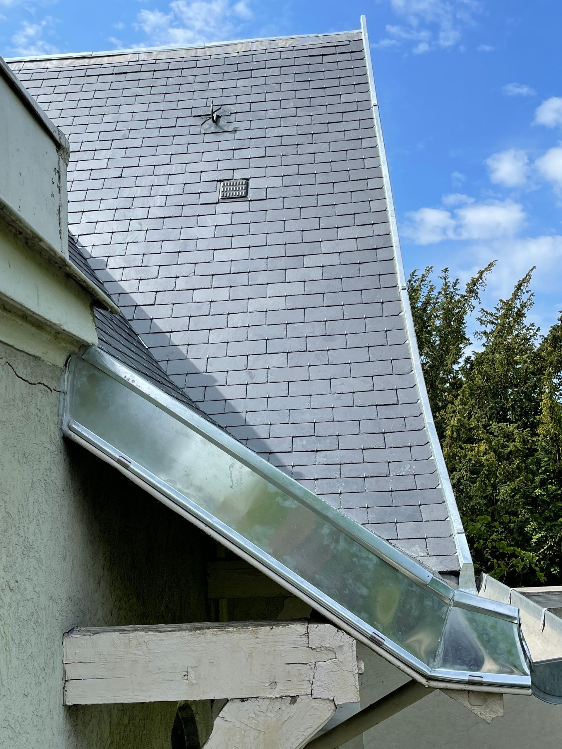 Une gouttière métallique installée le long du bord d'un toit en bardeaux gris sur un bâtiment, avec un ciel bleu en arrière-plan.