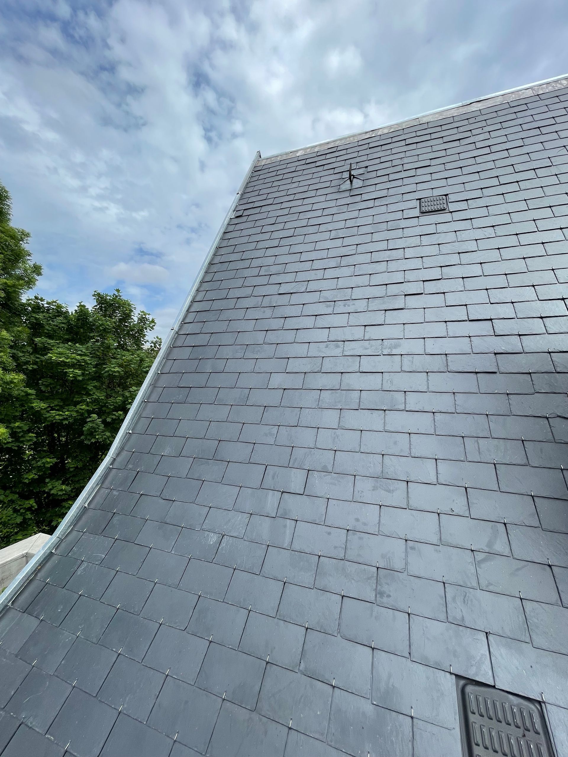 Toit d'ardoise d'un bâtiment, incliné vers le haut, avec un ciel nuageux en arrière-plan.