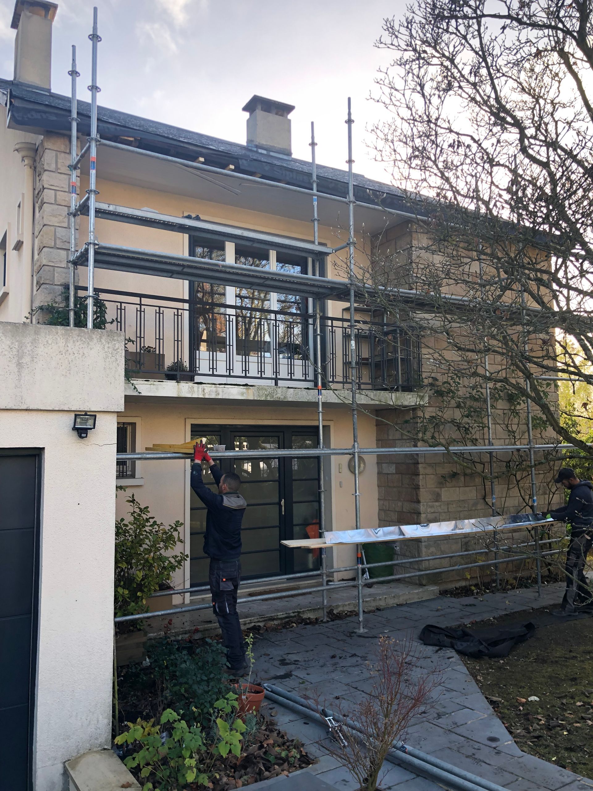 Des ouvriers sur un échafaudage à côté d'une maison à deux étages, en train d'installer un revêtement.
