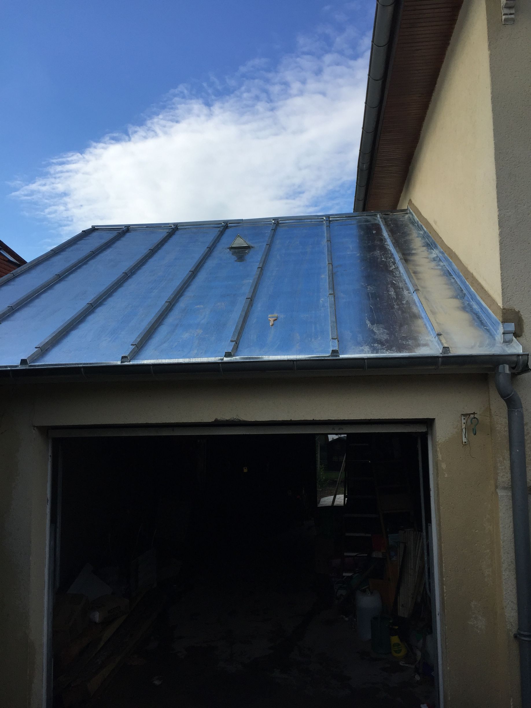 Toit de garage en panneaux métalliques, intérieur sombre, ciel bleu nuageux.