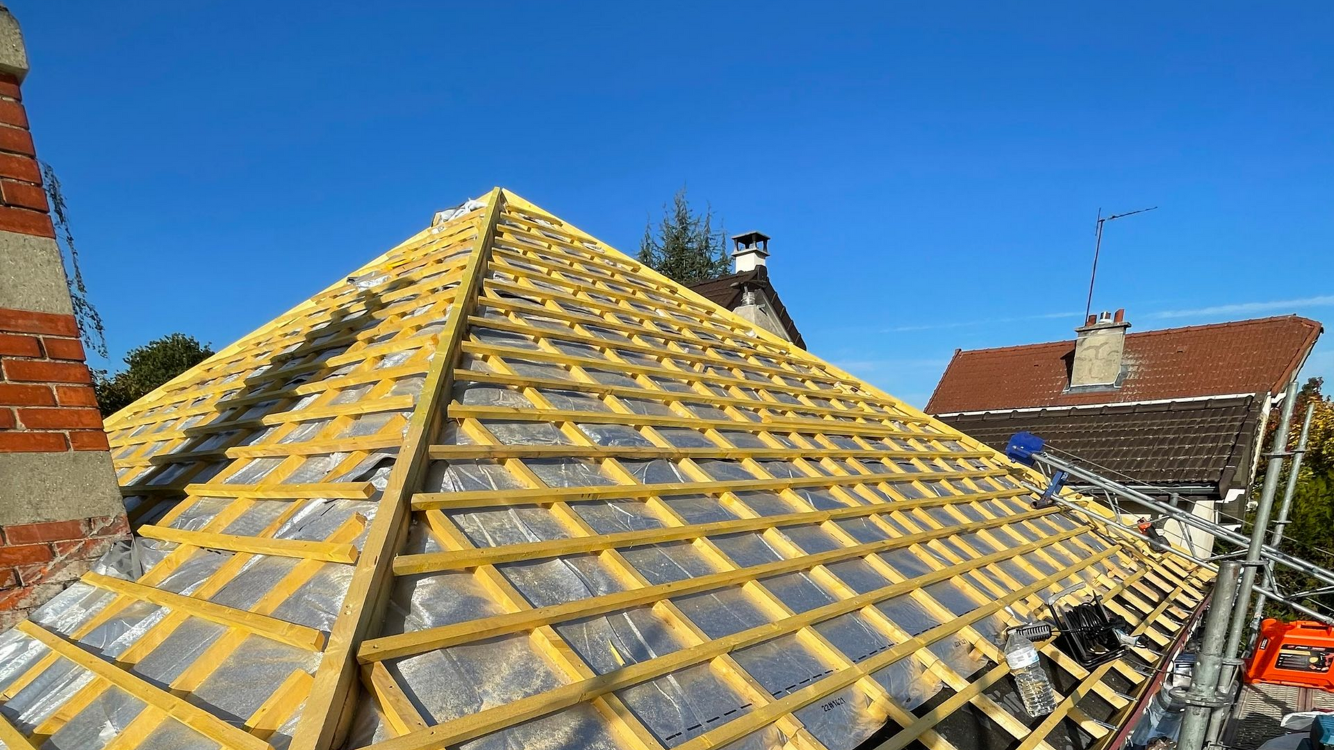 Toiture en construction, poutres en bois et isolation sur un toit en pente, se détachant sur un ciel bleu.