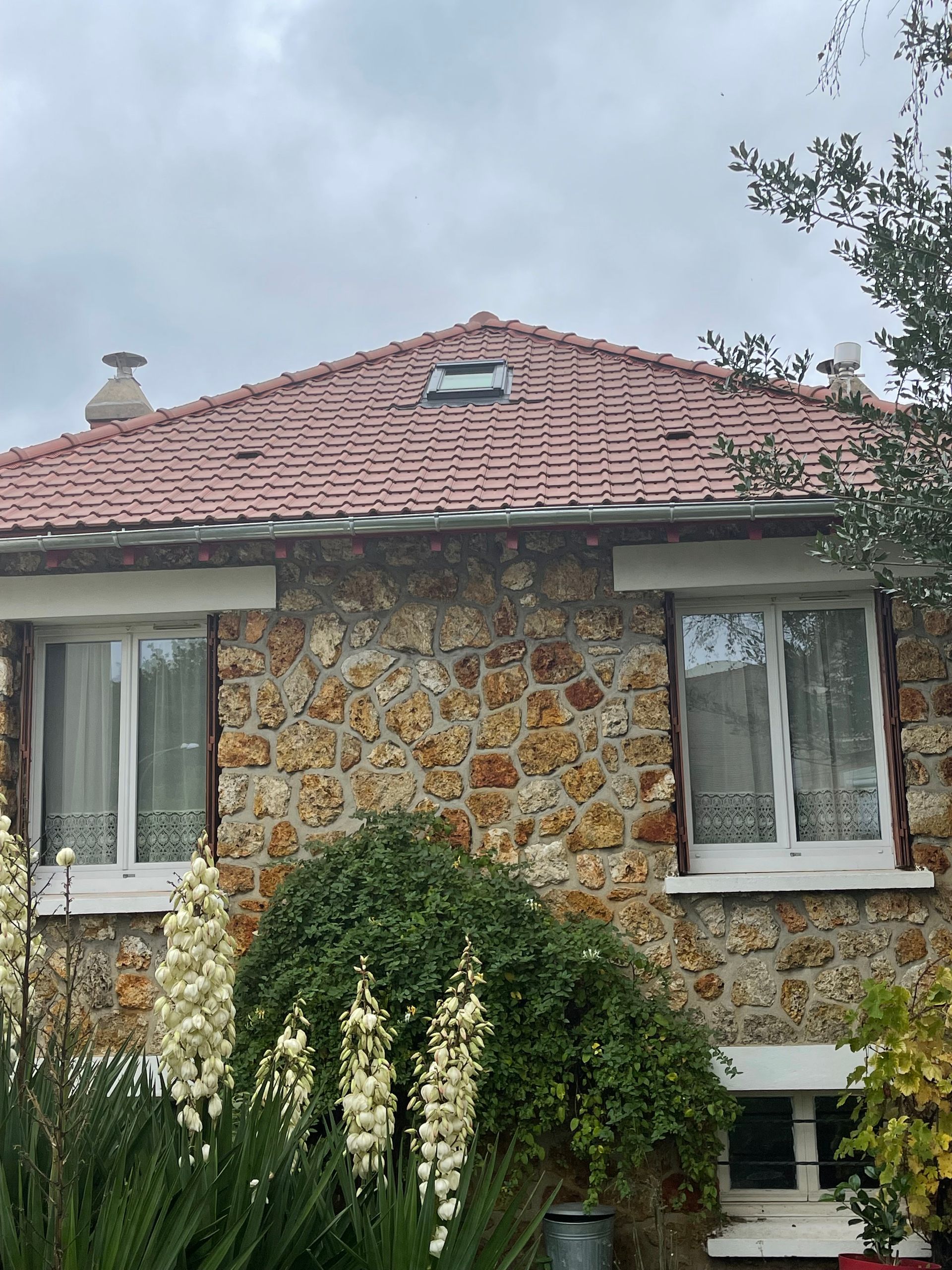Vue d'un toit sombre et incliné avec une gouttière métallique centrale. Le ciel est lumineux.