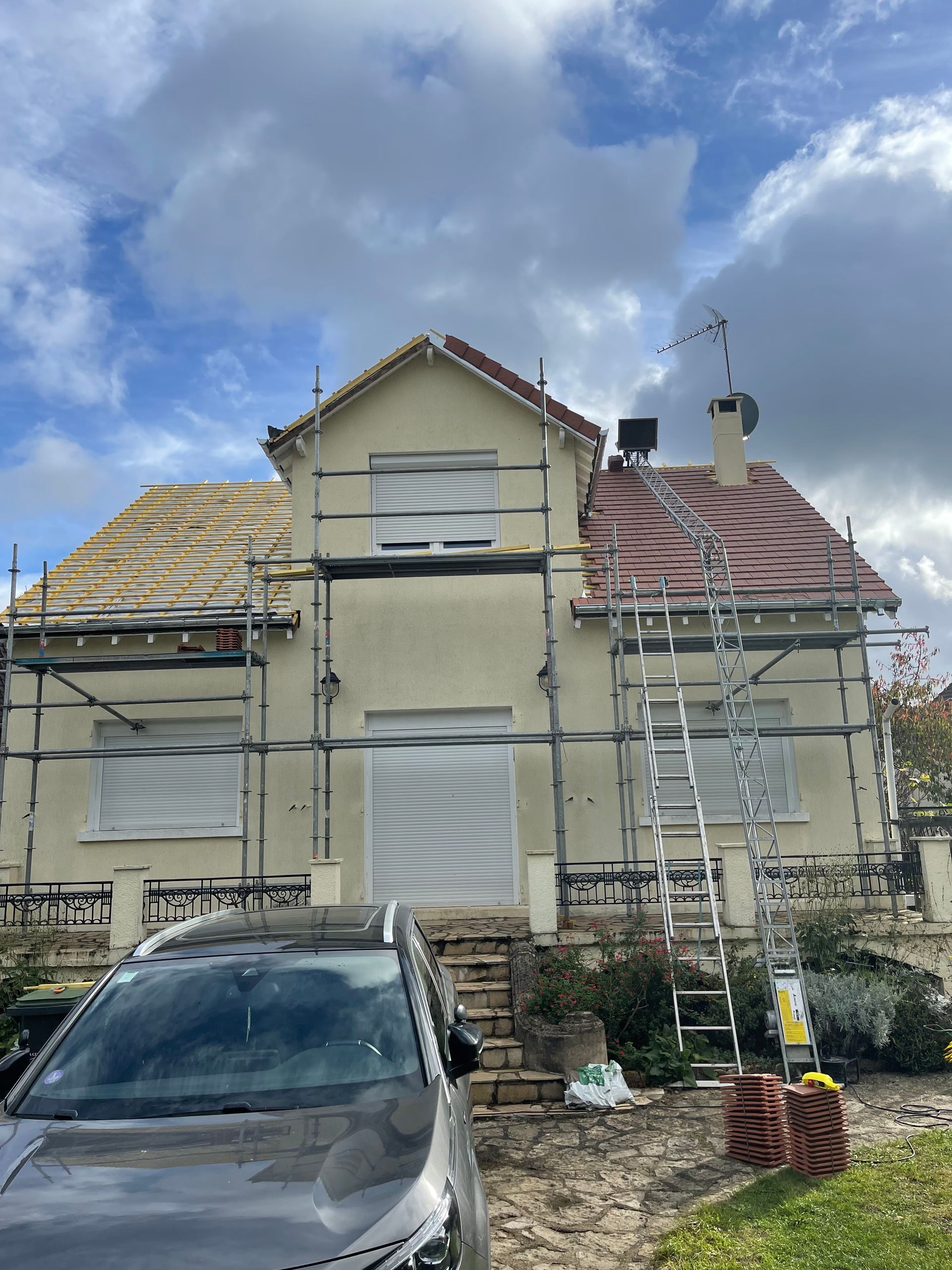 Maison avec échafaudages et toiture partiellement refaite sous un ciel nuageux.