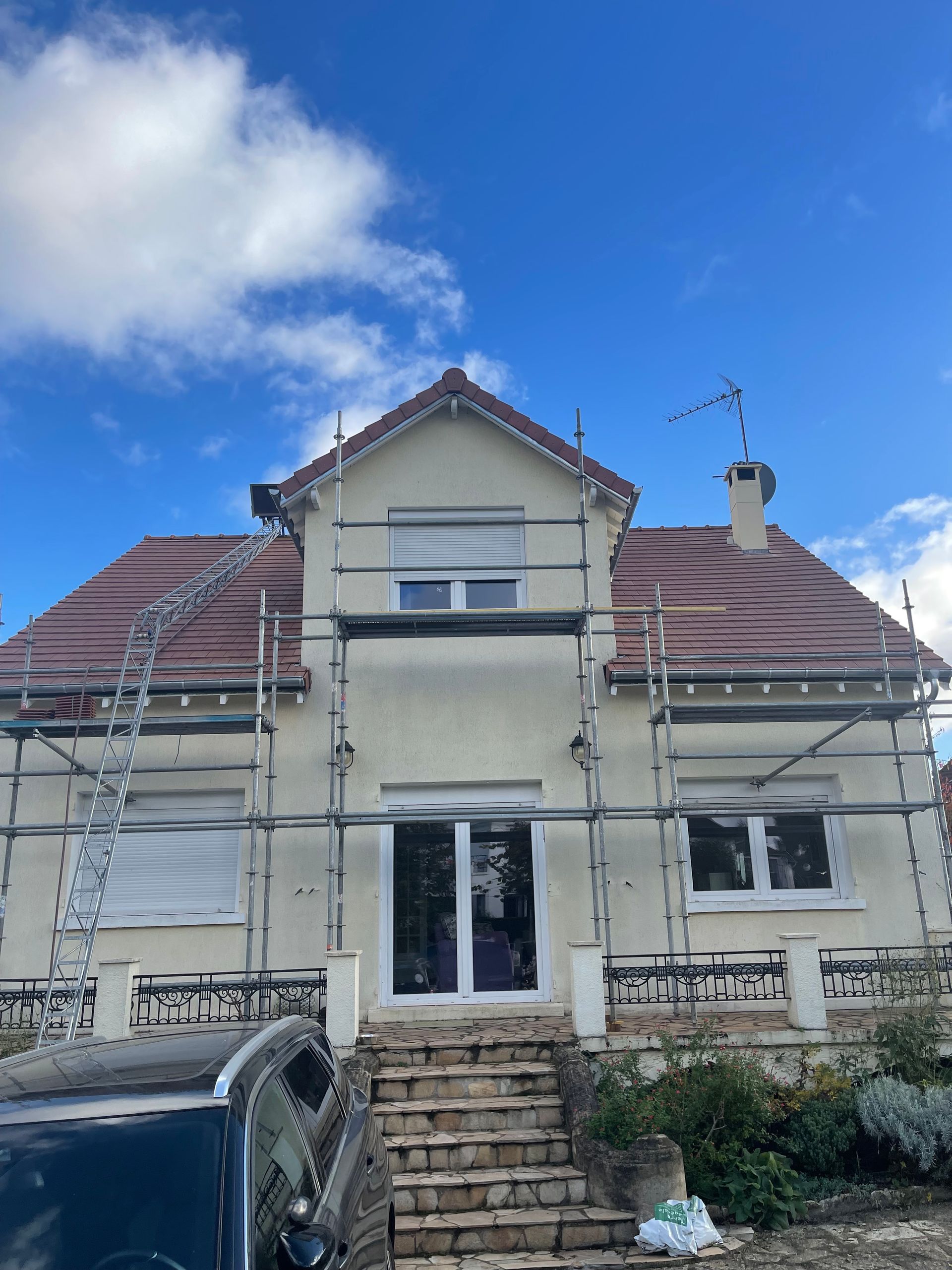 Maison en rénovation avec échafaudages, toit de tuiles rouges et ciel bleu.