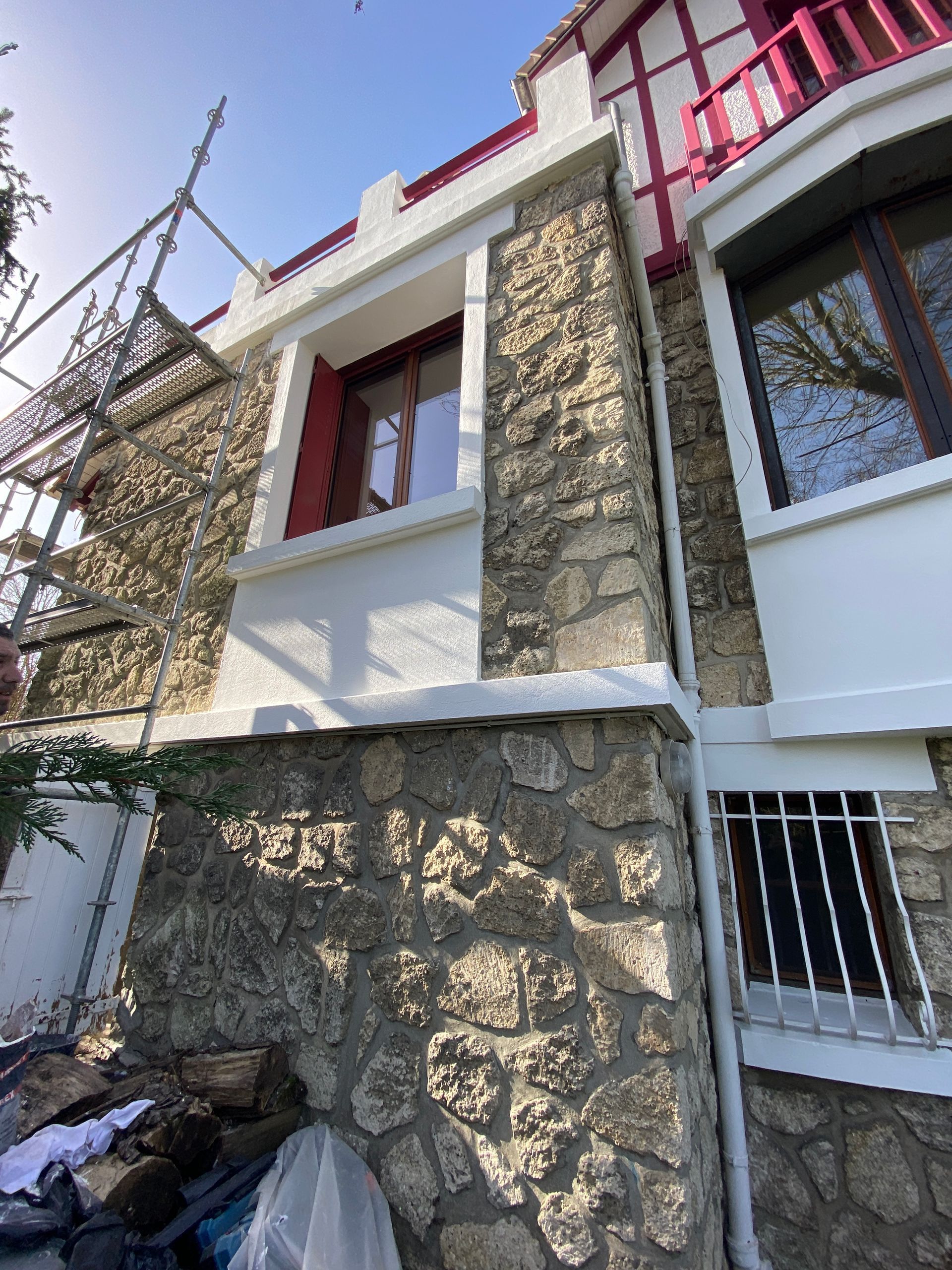 Façade en pierre et blanche avec des ornements rouges et des échafaudages.