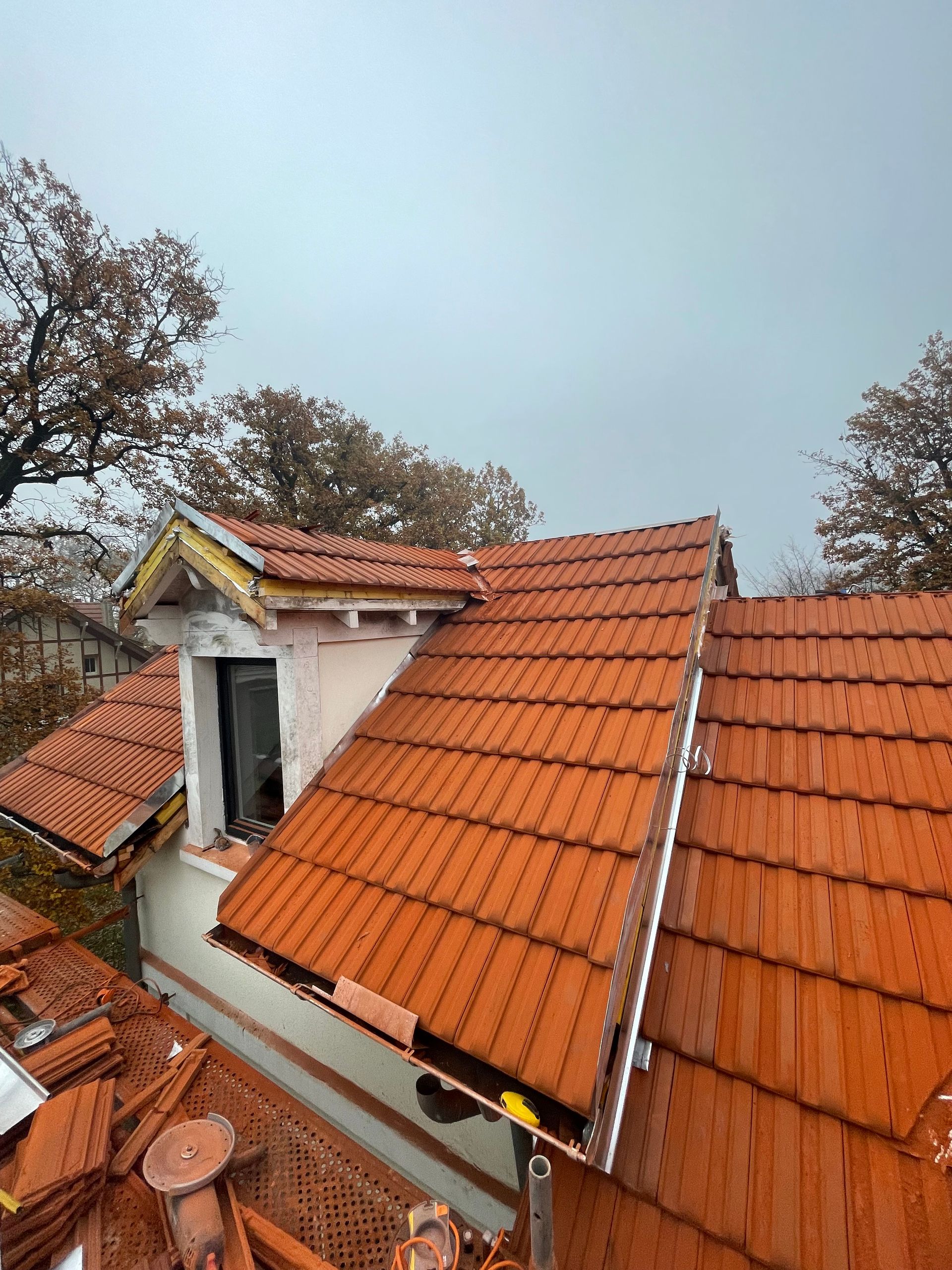 Toit de tuiles rouges d'une maison en construction ; une fenêtre et un ciel nuageux sont visibles.