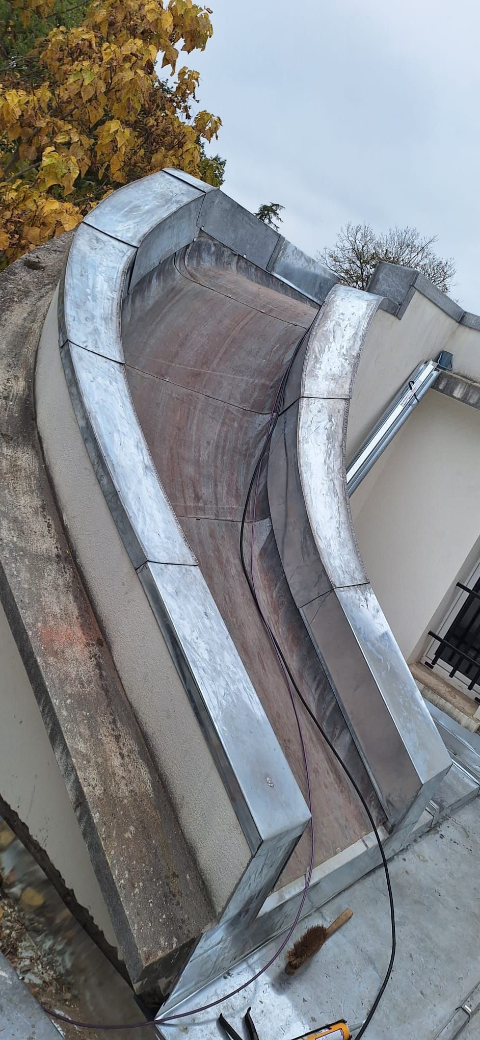 Réparation de gouttières sur un bâtiment. Toiture en tuiles rouges avec échafaudages. Mur blanc, gouttière marron et mousse isolante.