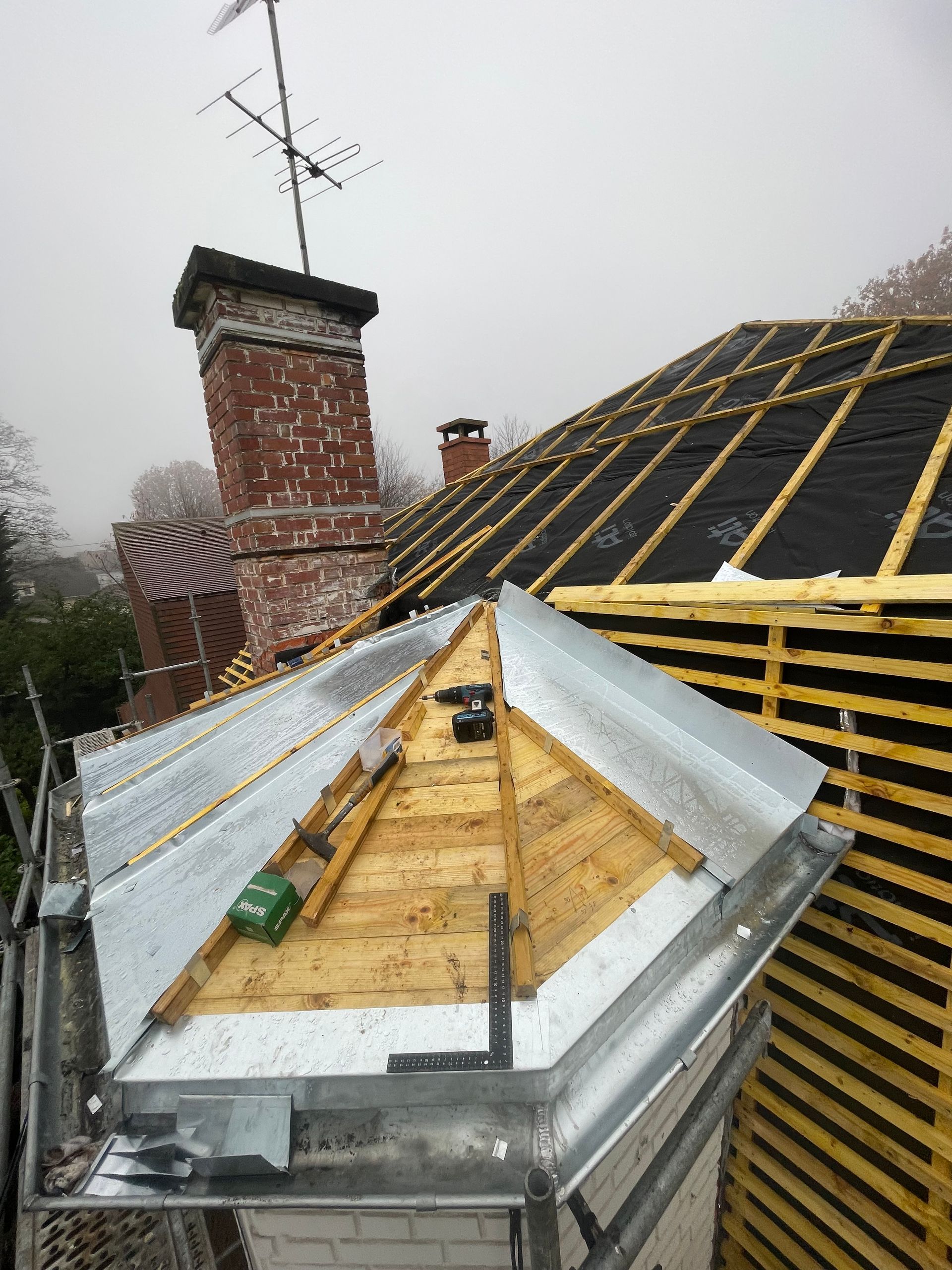 Travaux de toiture en cours : chevrons en bois, papier goudronné et solins métalliques près de la cheminée par temps de brouillard.