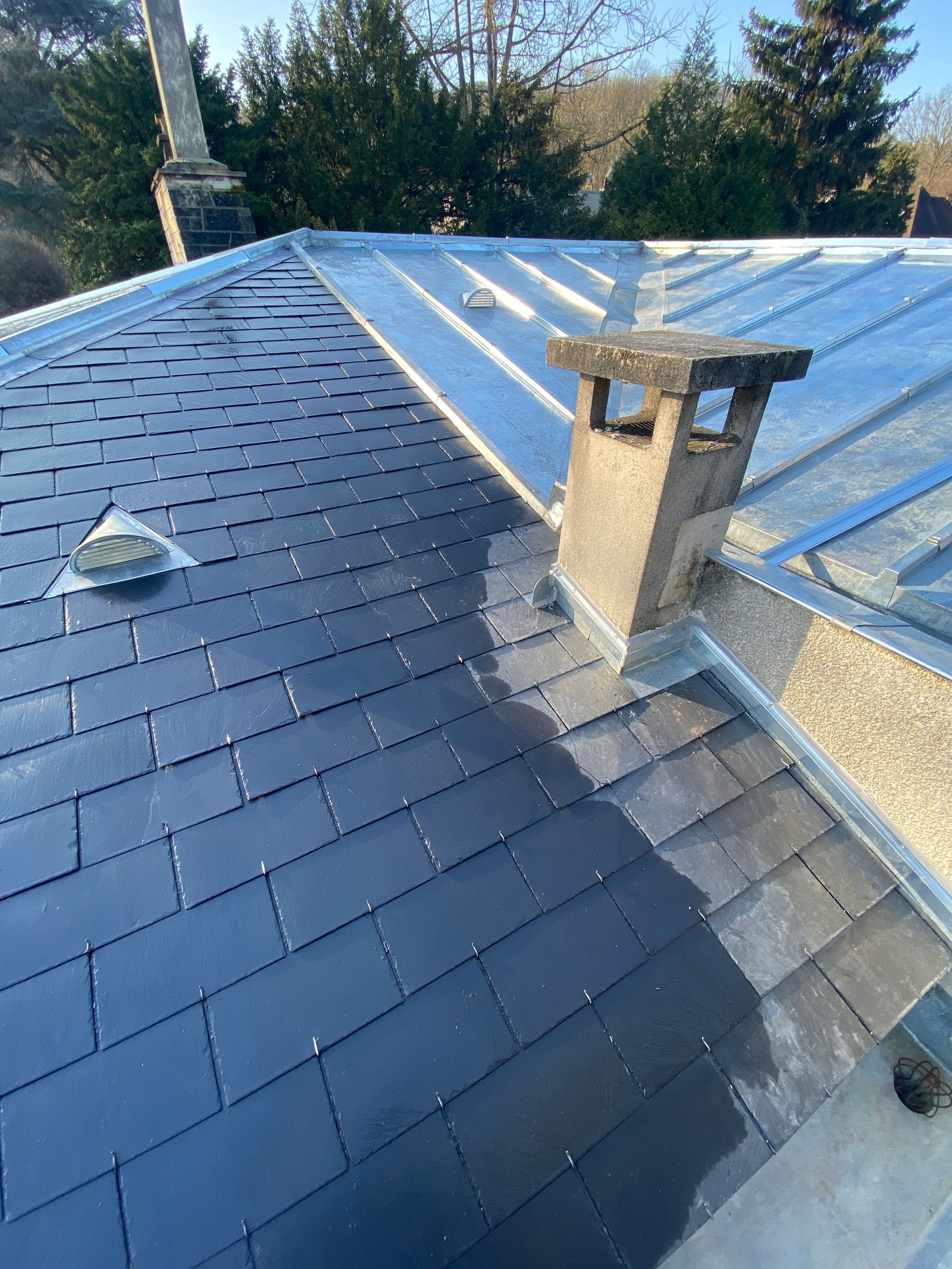 Toiture en ardoise et panneaux métalliques, avec une cheminée en briques.