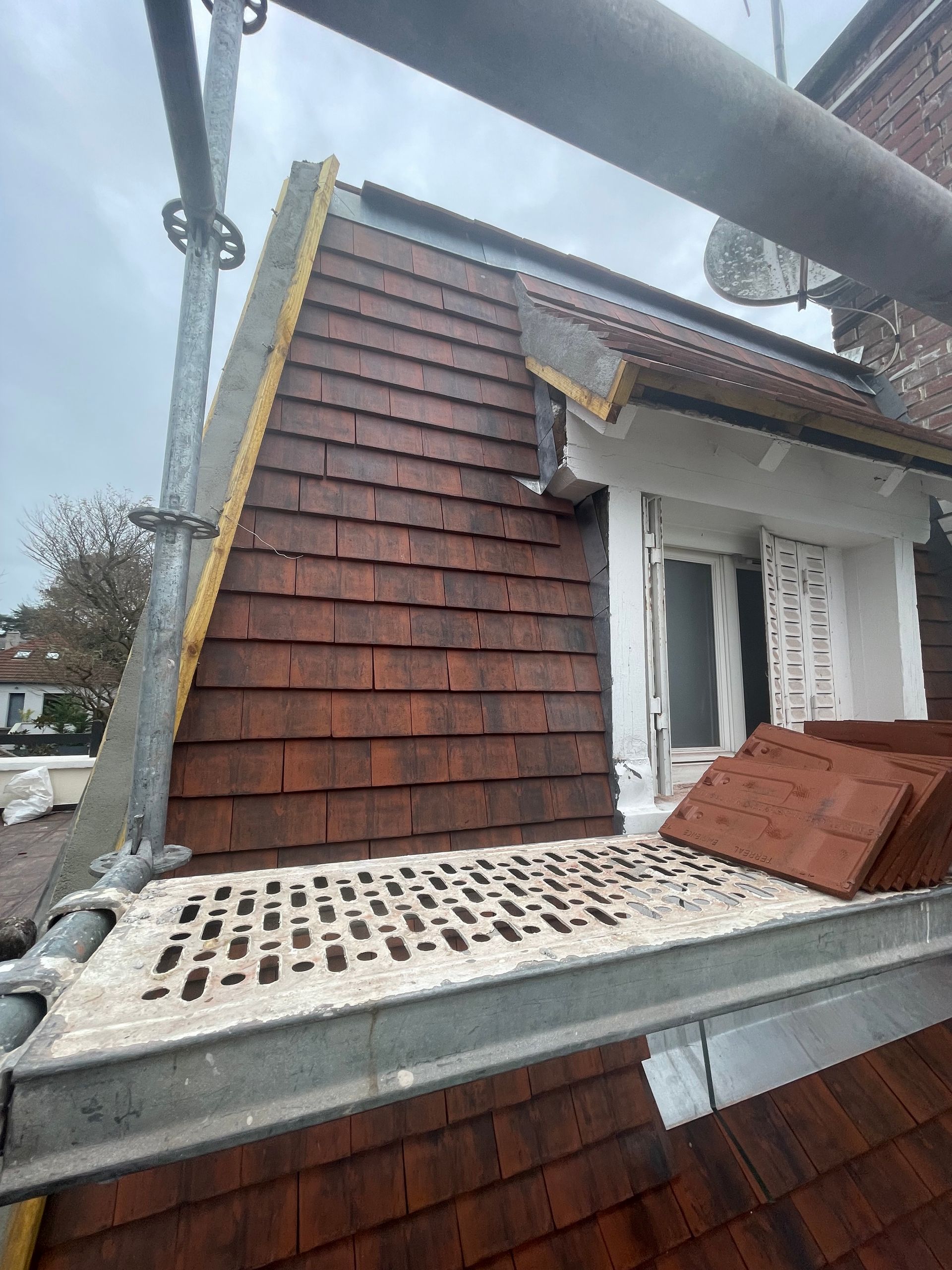 Pose d'un toit en bardeaux bruns, échafaudages visibles.
