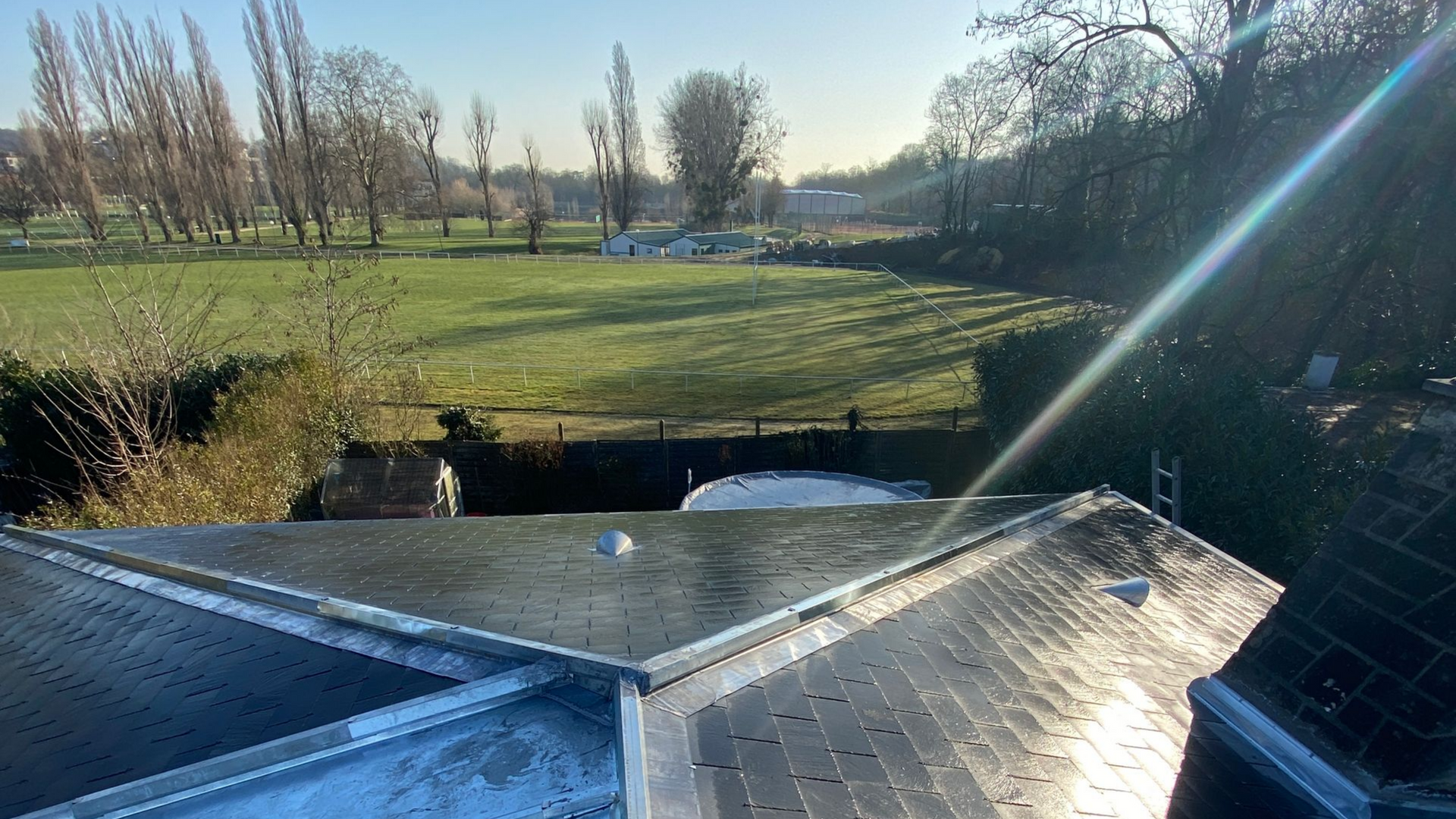 Vue depuis un toit, donnant sur un champ verdoyant et ensoleillé parsemé d'arbres dénudés.