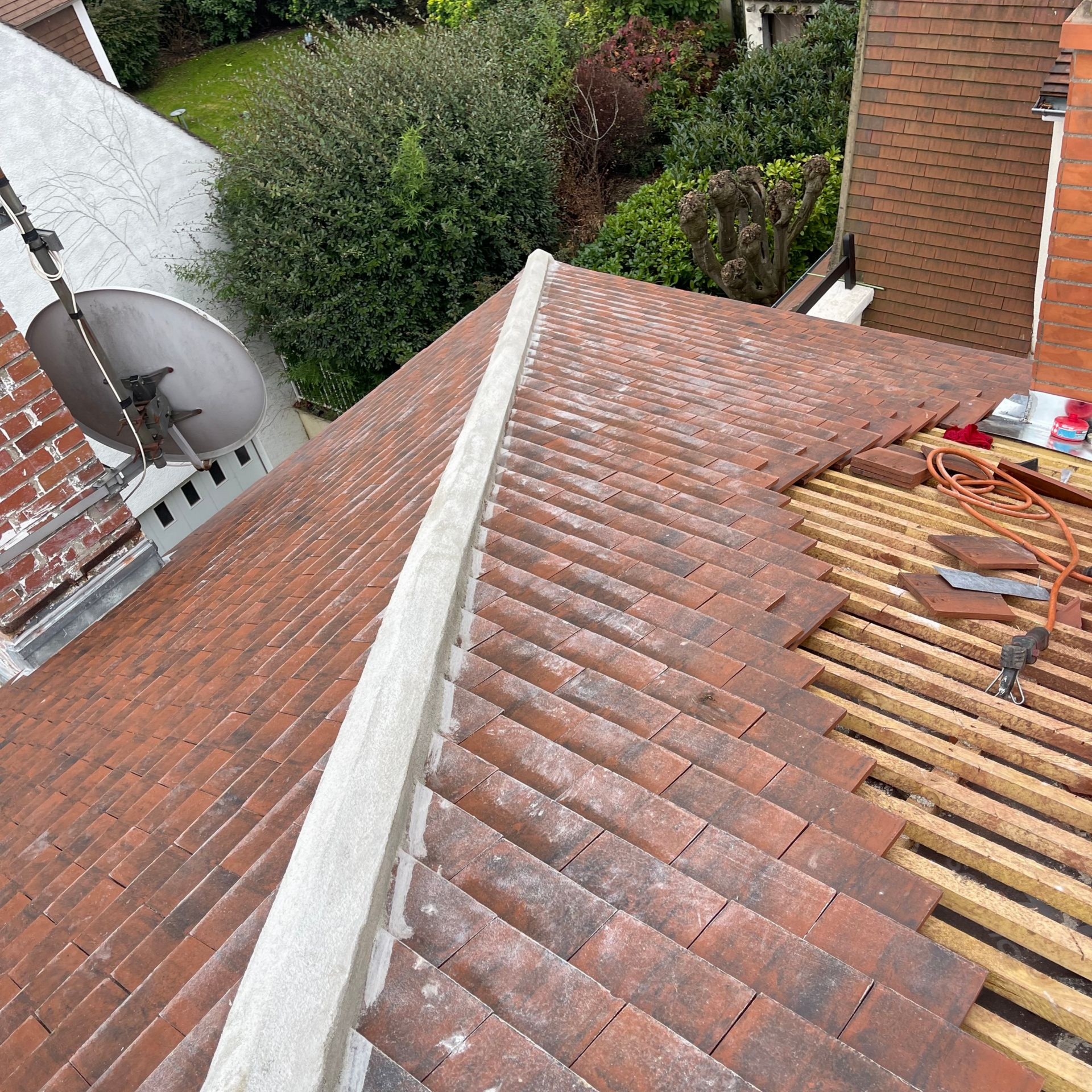 Toiture en tuiles orange en cours de réparation ; poutres apparentes. La lumière vive du soleil illumine la scène.