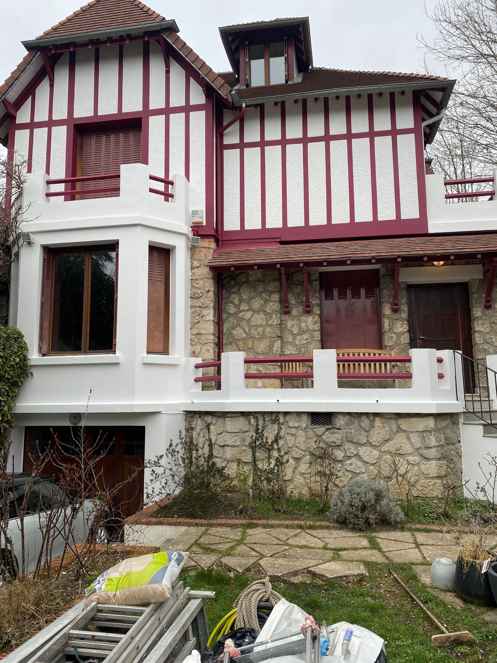 Maison à deux étages avec des éléments en bois rouge et blanc, une façade en pierre et un petit balcon.