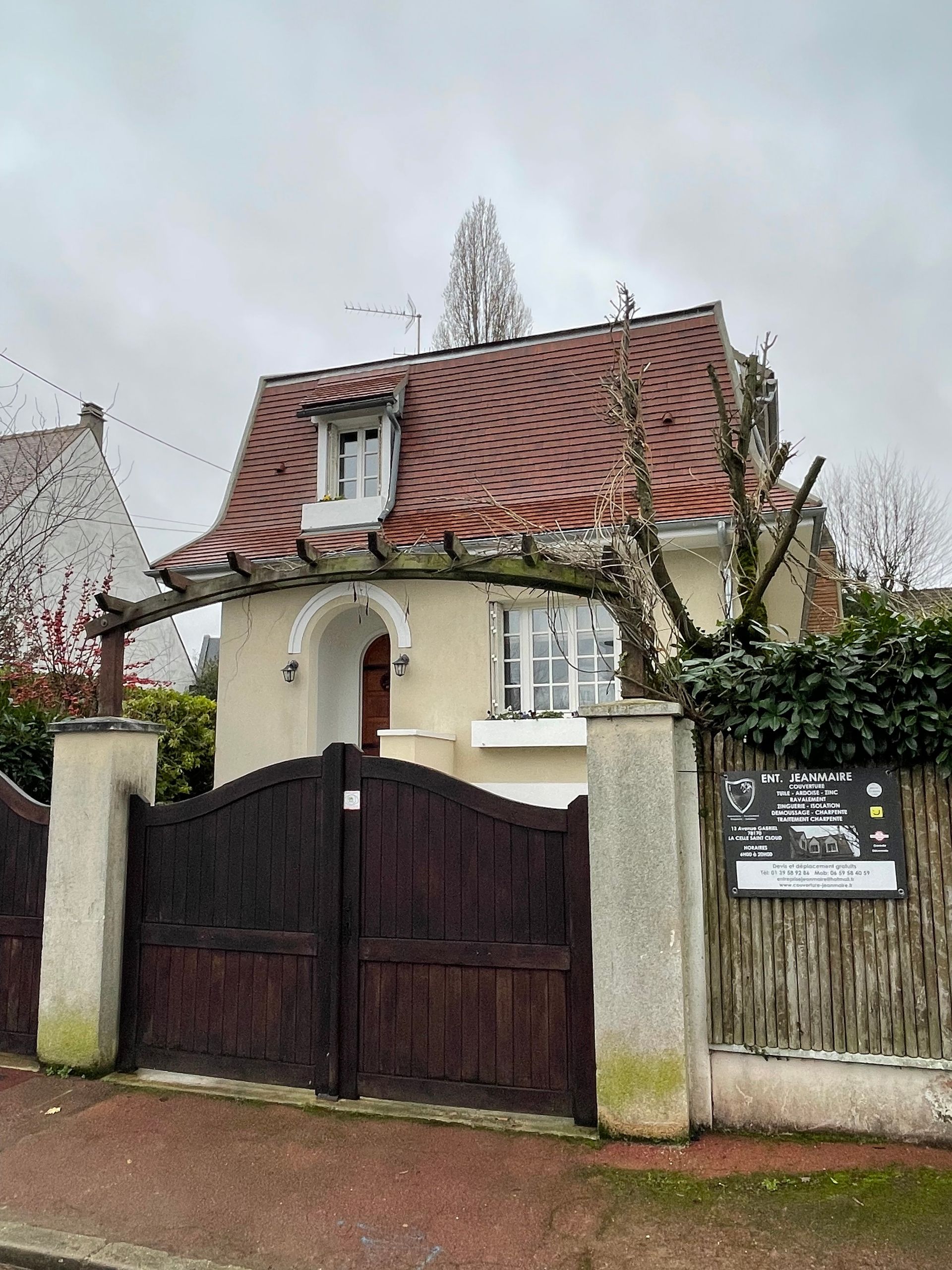Une maison avec une toiture neuve, un arbre dans le jardin et un portail noir