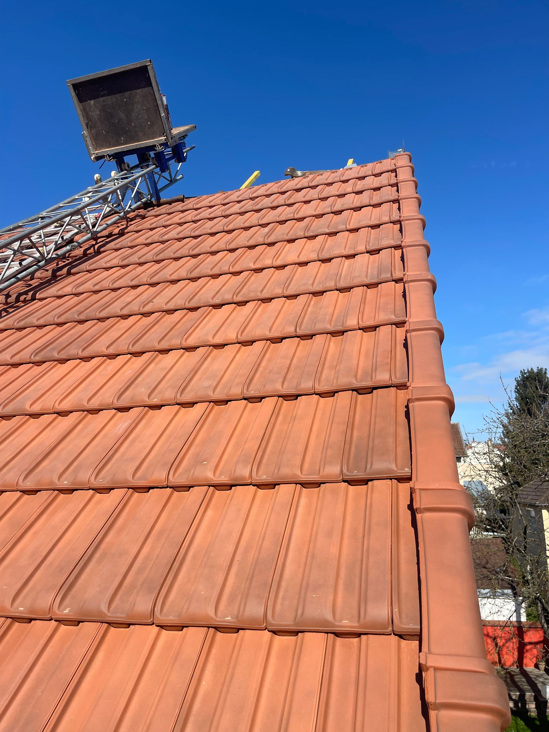 Toit de tuiles rouges avec une échelle se détachant sur un ciel bleu azur.