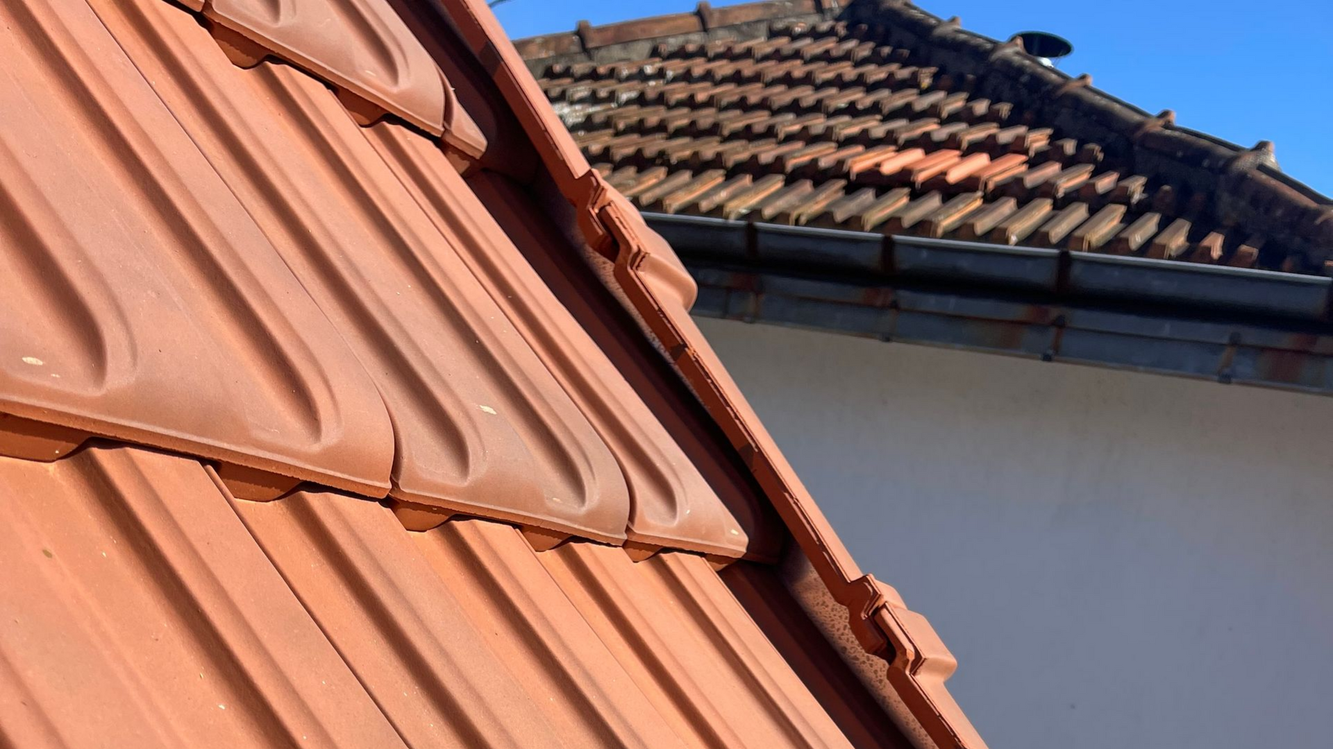 Gros plan sur des tuiles de toit en terre cuite à motif nervuré, se chevauchant sur un ciel bleu ensoleillé.