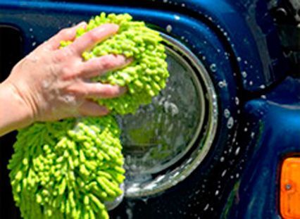 Una persona está lavando un coche azul con una esponja verde.