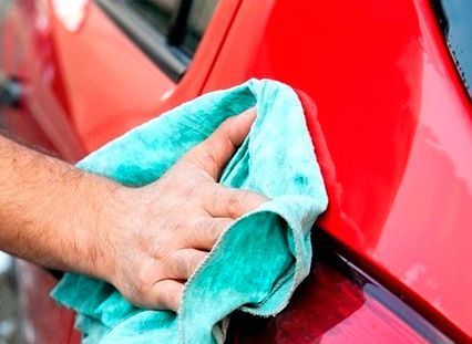 Una persona está limpiando un coche rojo con una toalla.