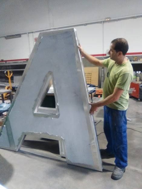 Un hombre con una camisa verde sostiene una gran letra de metal A