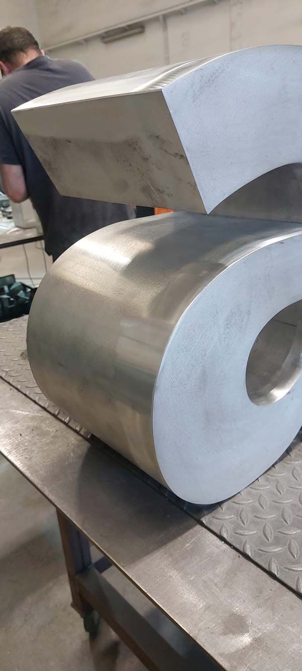 Dos grandes rollos de metal plateado y una pieza metálica cuadrada sobre una mesa de taller.