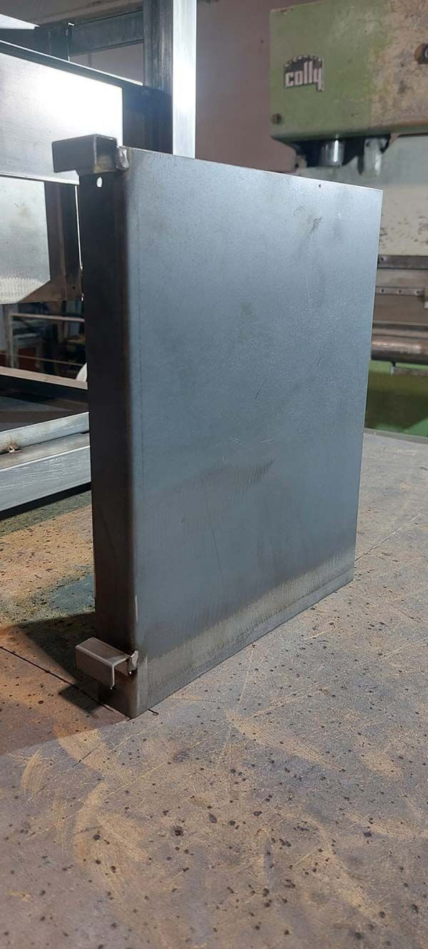 Una gran lámina de metal gris permanece de pie en un taller industrial, sobre un suelo polvoriento.