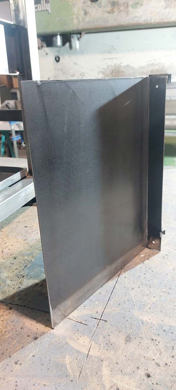 Una lámina de metal negro colocada en posición vertical sobre un suelo de hormigón en un taller industrial.