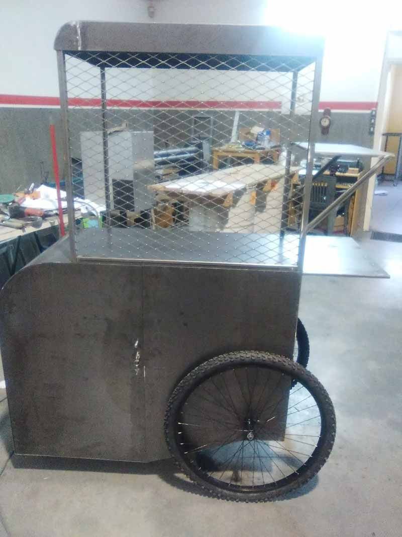 Carro metálico con tapa de malla y una sola rueda en el pasillo de un taller industrial.