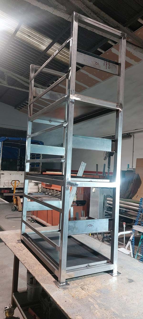 Estructura alta de estanterías metálicas en un taller, con herramientas y equipos en los estantes inferiores.