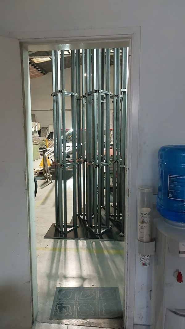 Pasillo estrecho con una puerta de seguridad metálica, paredes blancas y un dispensador de agua azul a la derecha.