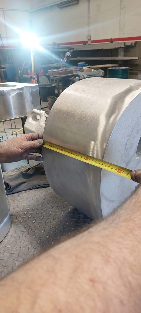 Persona midiendo una pieza cilíndrica metálica grande con una cinta métrica en un taller.