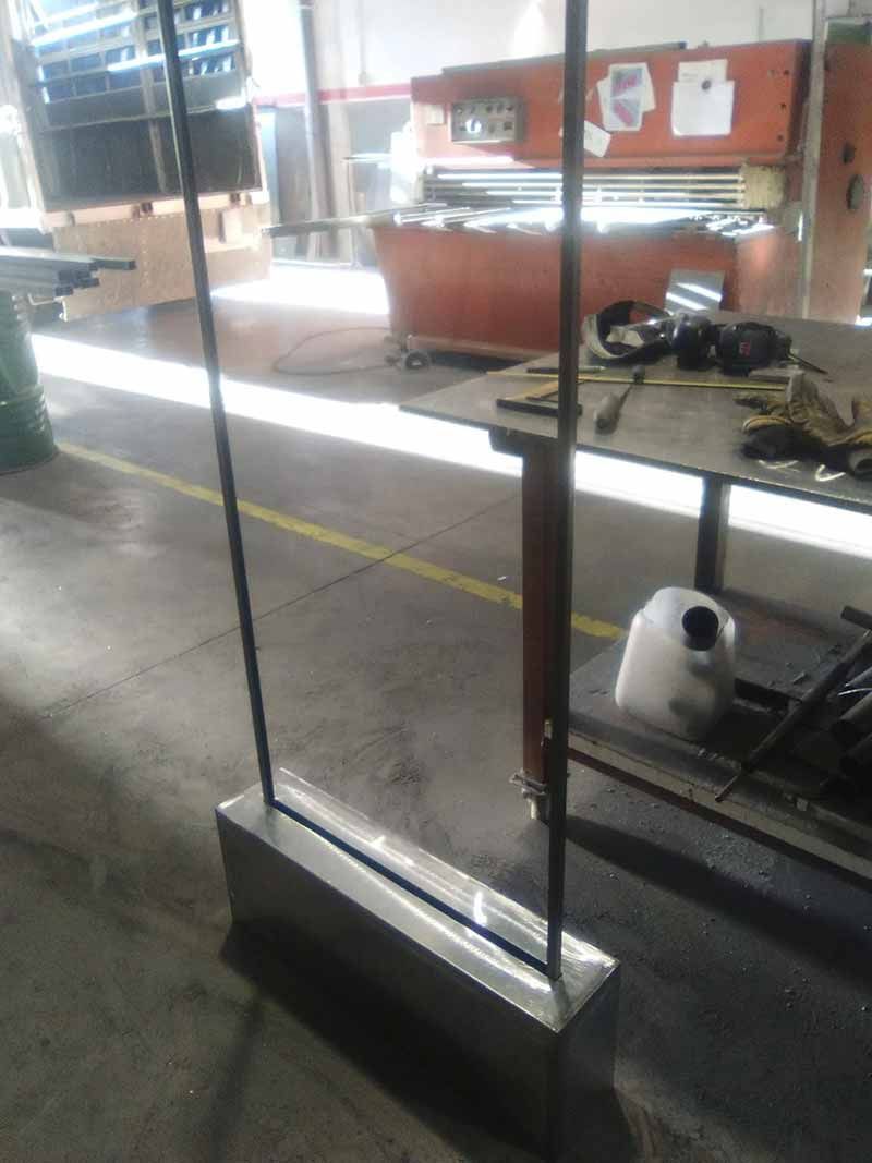 Mampara de cristal en un taller, con herramientas y equipos en estantes detrás.