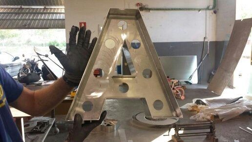 Un hombre que lleva guantes negros sostiene una gran letra de metal 