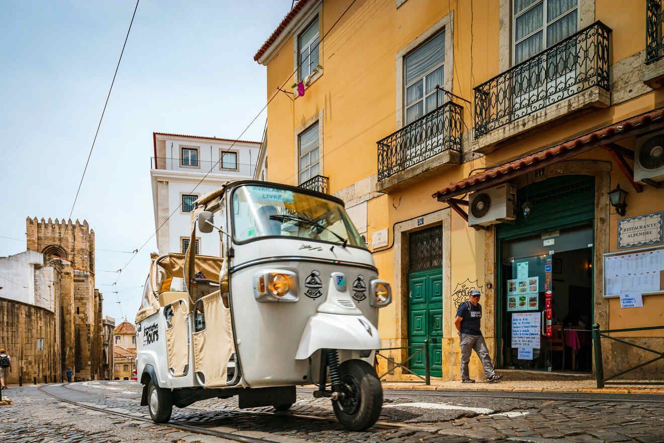 A white three wheeled vehicle is parked in front of a yellow building.