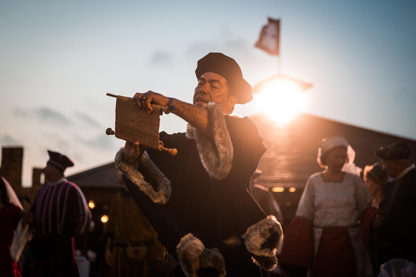 A man in a medieval costume is playing a musical instrument in front of a crowd.