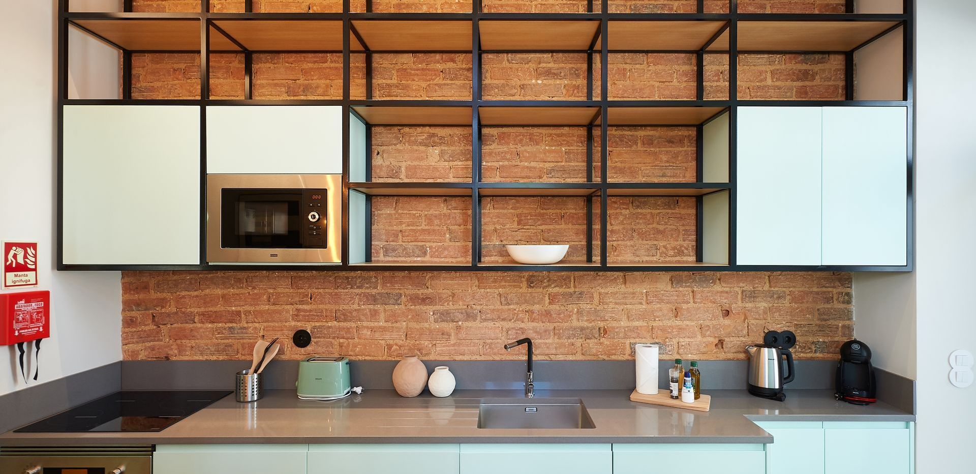 a kitchen with a brick wall , white cabinets , a sink , and a microwave .