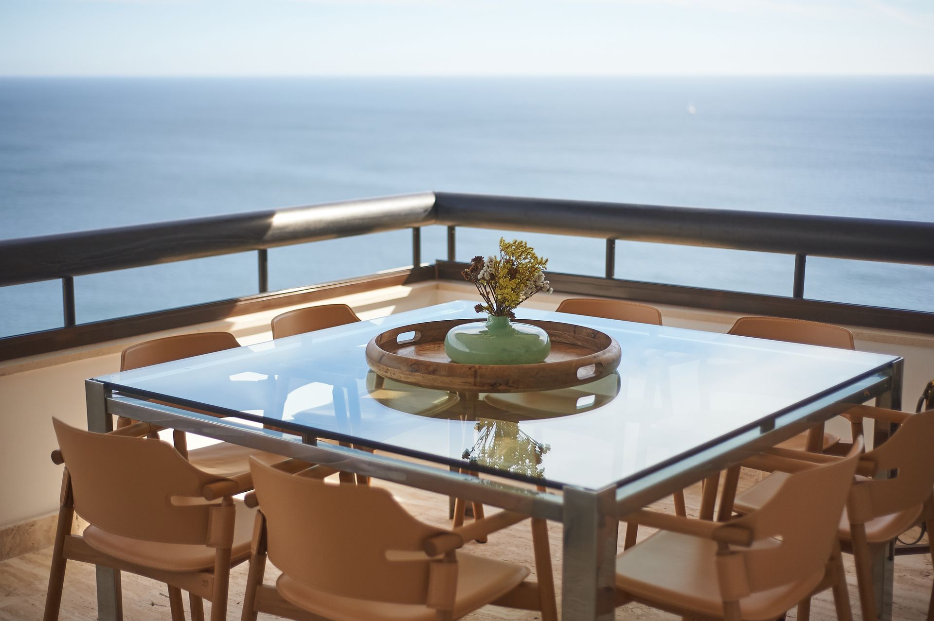 a glass table and chairs on a balcony overlooking the ocean