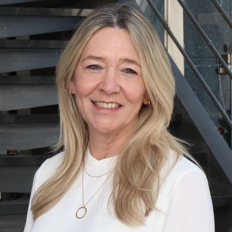 A woman in a white shirt is smiling in front of a set of stairs.