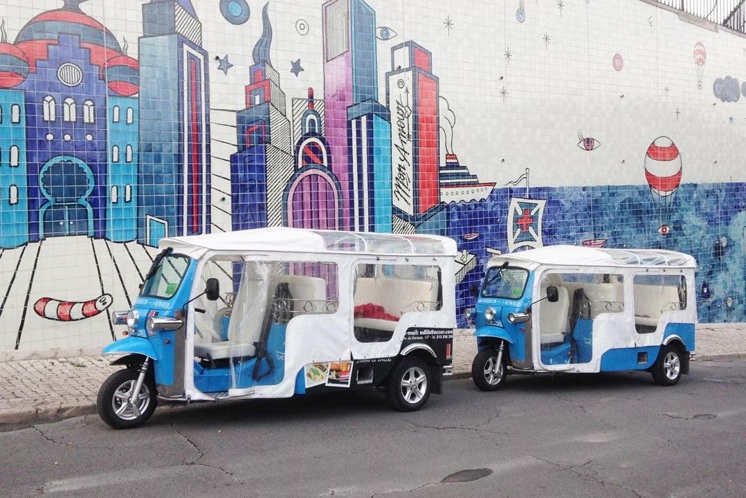 Two rickshaws are parked on the side of the road in front of a mural on a wall.