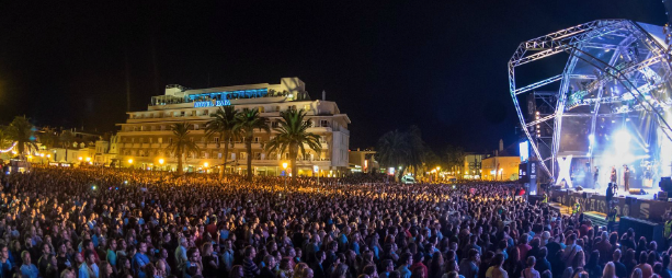 A large crowd of people are watching a concert at night.