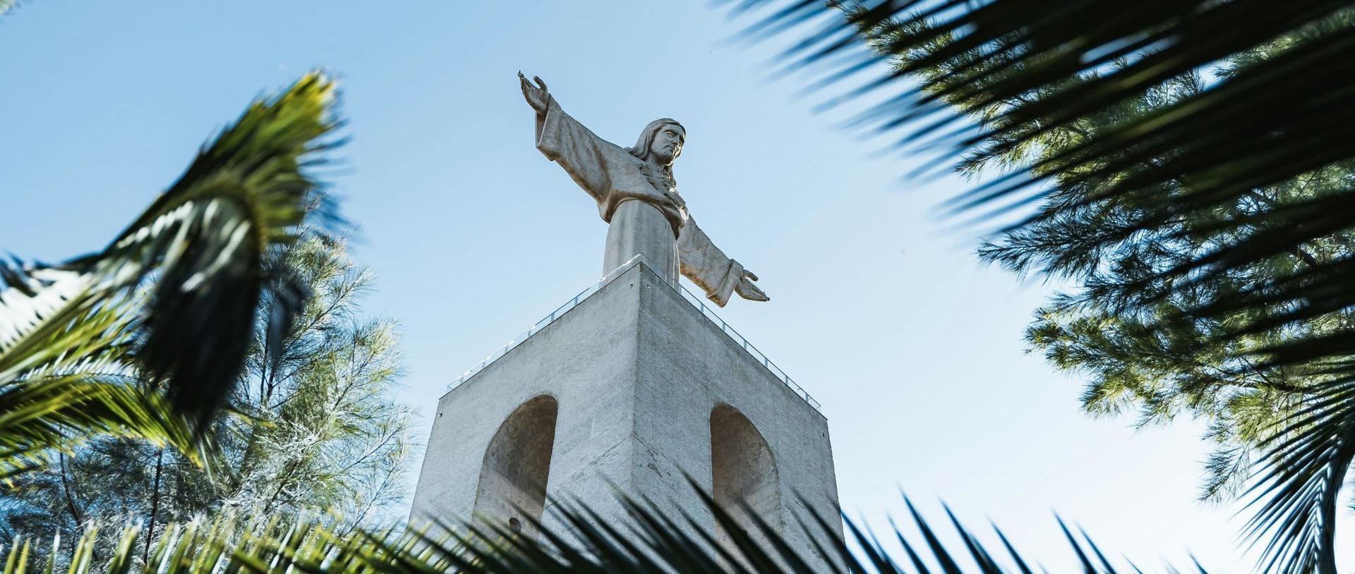 A statue of jesus is standing on top of a building surrounded by palm trees.