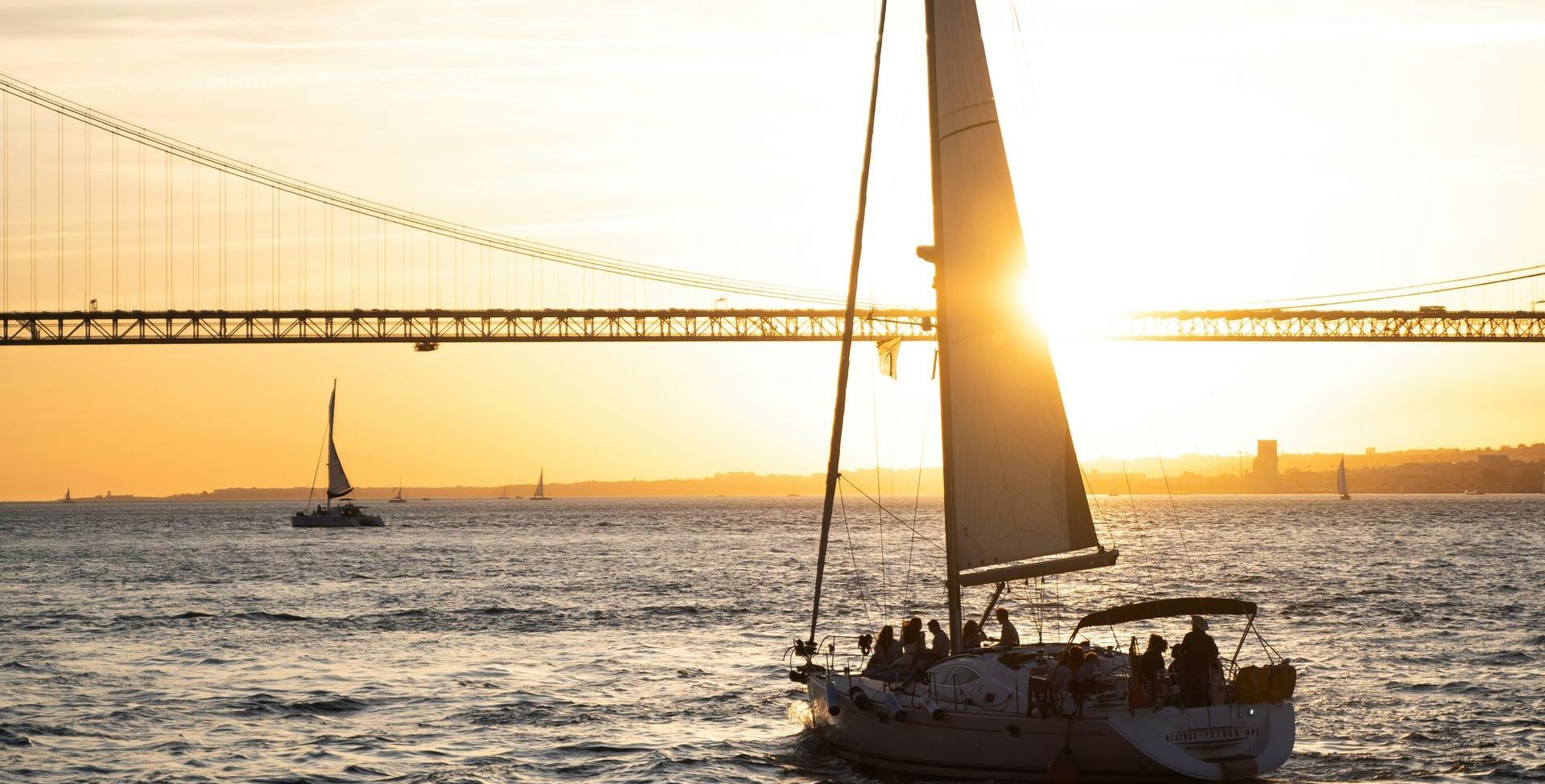 A sailboat is floating on top of a body of water with a bridge in the background.