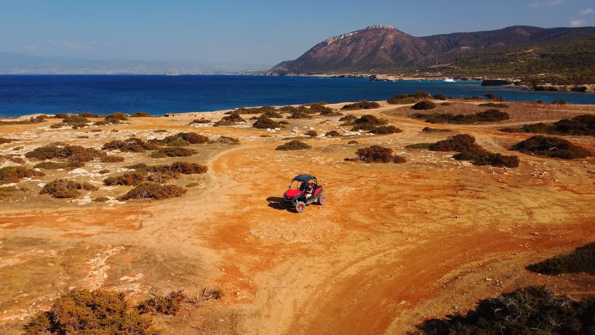 An aerial view of a person riding an atv on a dirt road near the ocean.